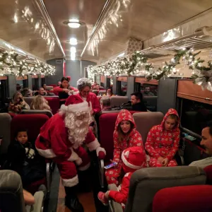Santa interacting with families on a festively decorated train with garlands and lights.