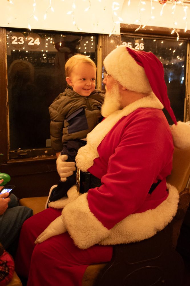 Child smiling at Santa Claus seated indoors with festive lights.