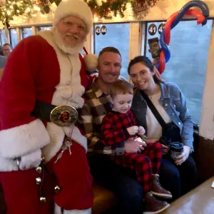 Santa with family on a decorated train with festive garland and lights.