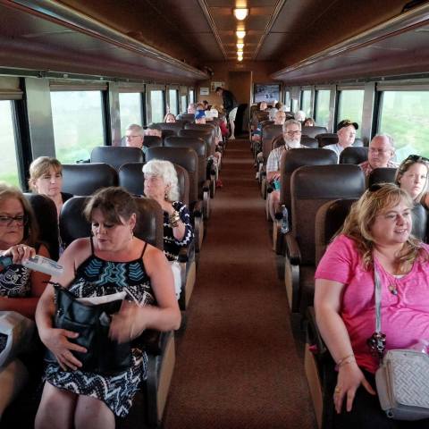Interior of a train car with seated passengers, mostly middle-aged, looking relaxed and engaged in conversation.