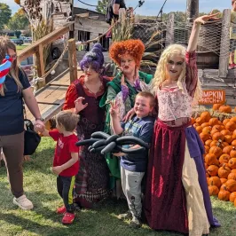 People in costumes posing with two children in front of a wooden ship and pumpkins.