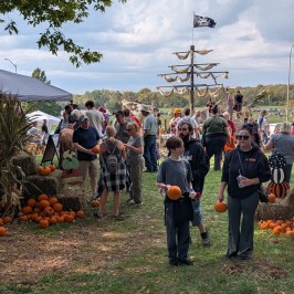 People at a pumpkin patch festival with a pirate ship and hay bales.
