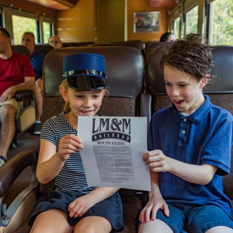 Two children in a train reading a route guide together.
