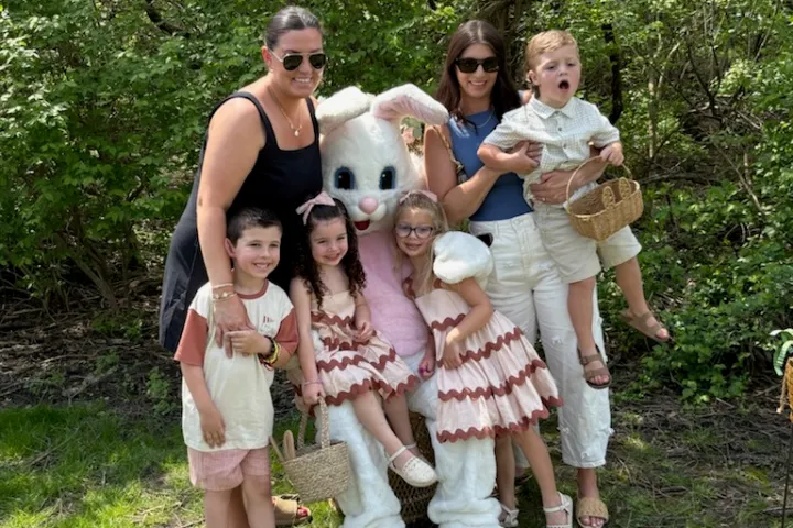 Two adults and four children posing with Easter Bunny outdoors.