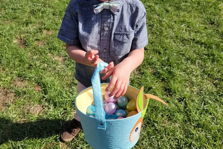 a little boy that is standing in the grass with an easter basket