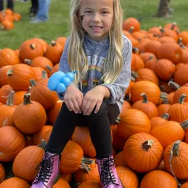 a little girl sitting on a pile of pumpkins