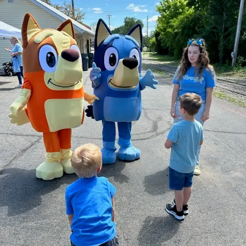 Two costumed characters and two children interacting outdoors on a sunny day.